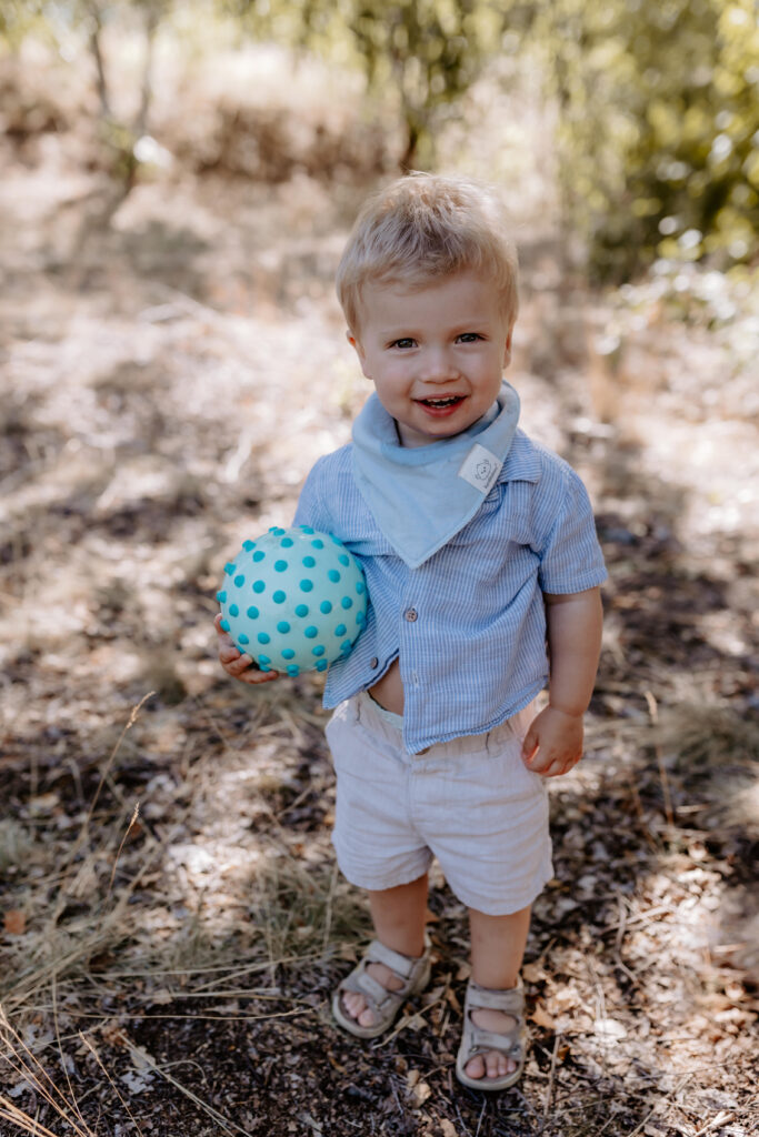 Sohn lacht in die Kamera und hat einen Ball in der Hand